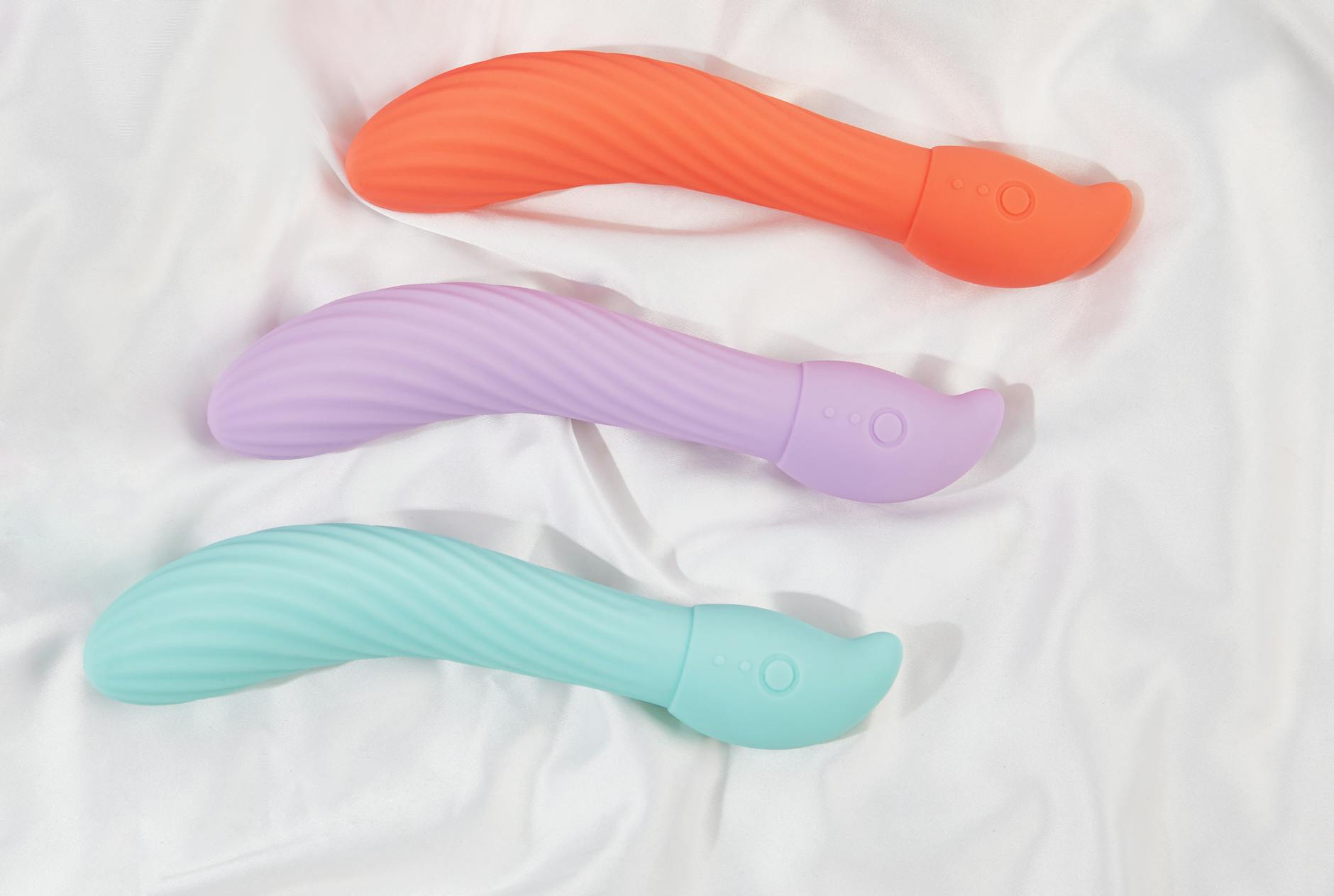 Three colorful clitoral vibrators on white fabric showing smooth texture and design detail.