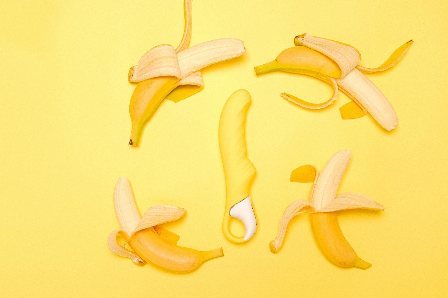 Yellow silicone lemon vibrator surrounded by peeled bananas on a bright yellow background